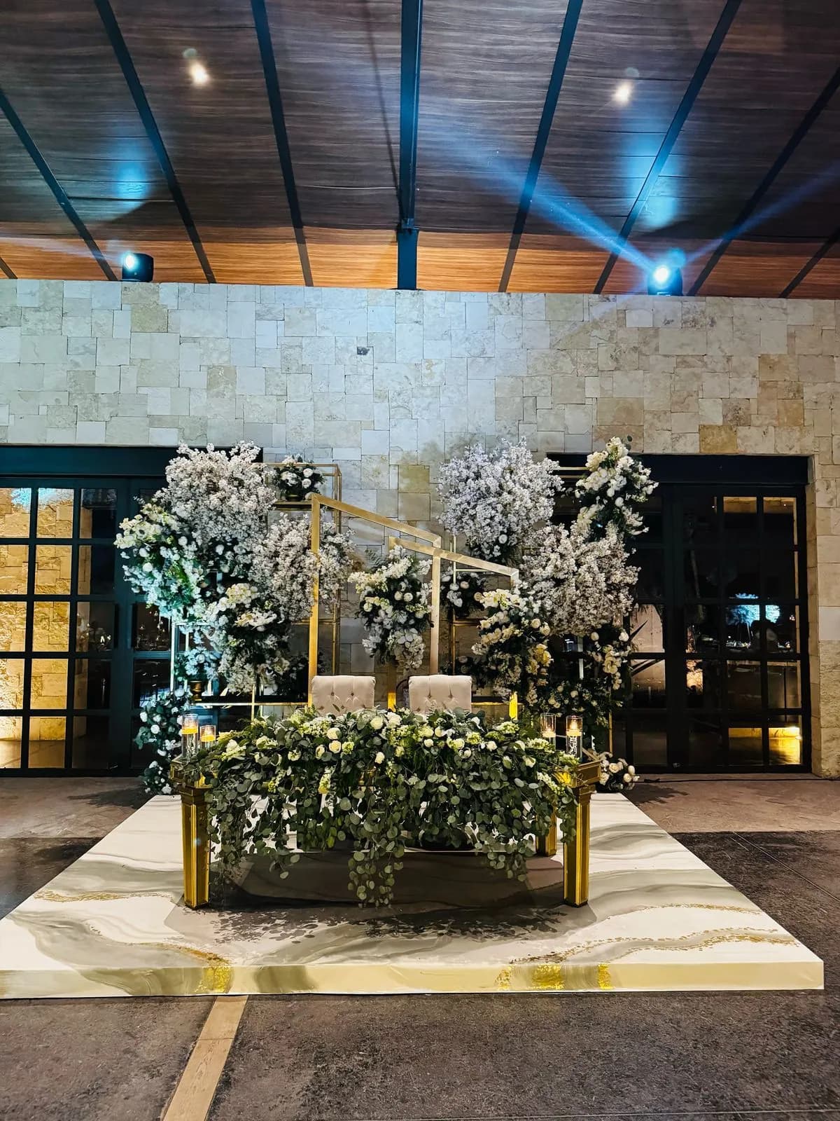 Mesa de novios con arreglos de flores blancas y estructura dorada