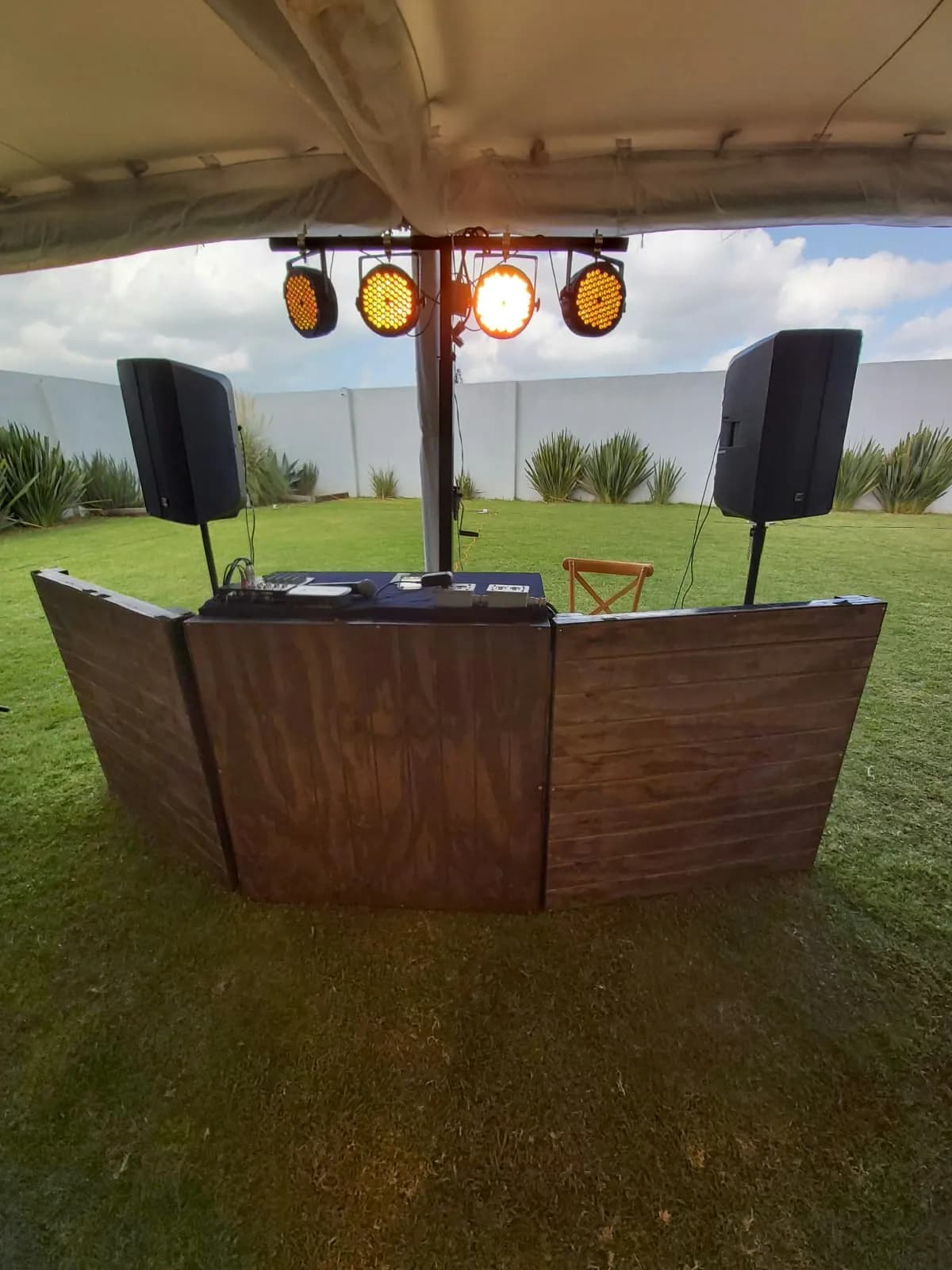Cabina de DJ de madera con bocinas e iluminación en un jardín