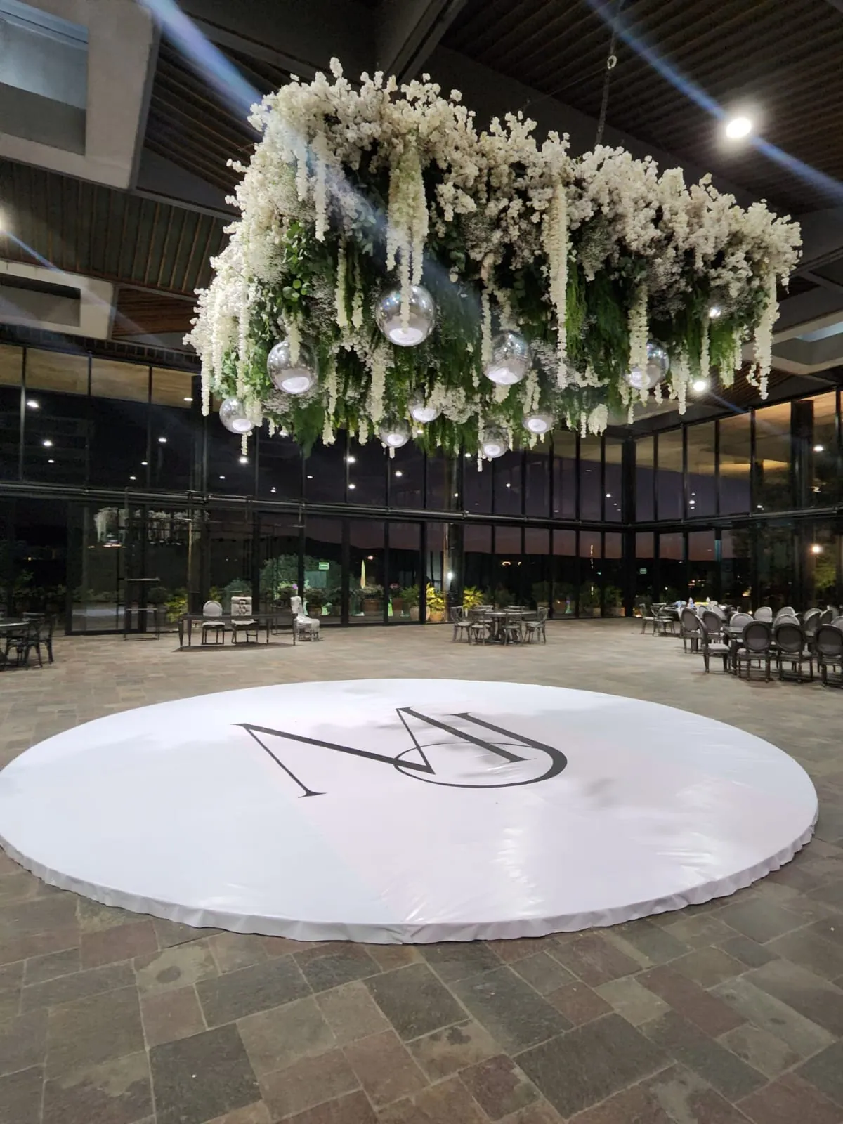 Pista circular blanca con monograma bajo un arreglo floral colgante